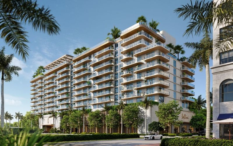 Luxury residential building exterior with warm wood-toned balconies, white facades, and tropical palm landscaping along a Boca Raton street