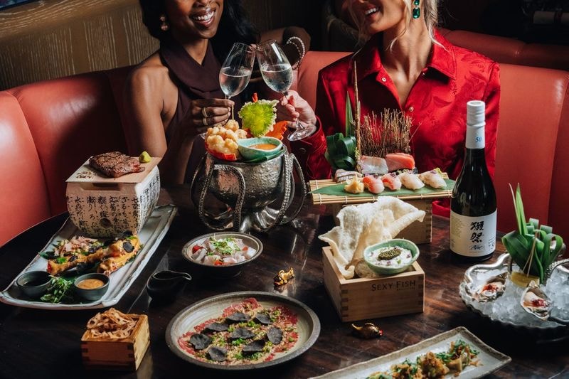 Two guests toasting with champagne over an elaborate spread of sushi, sashimi, tartares and premium seafood at Sexy Fish Miami
